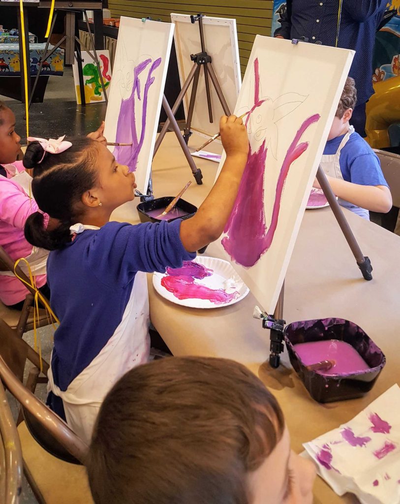 Kids painting on canvases with teachers.